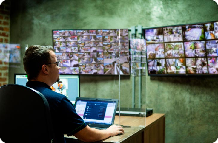 Homem sentado em frente a um computador observando uma tela com várias câmeras